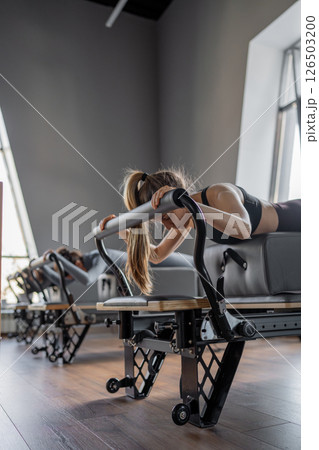 Womens doing Swan exercise on Pilates Reformer for the chest and back muscles, focusing on flexibility, strength, and control with determination 126503200