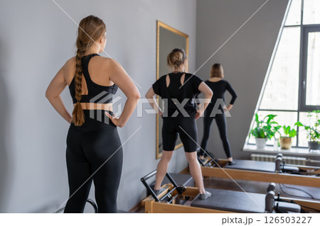 Young caucasian women exercising on pilates reformers in a bright studio. Their workout focuses on core strength and flexibility in a modern fitness environment. Young caucasian women exercising on pilates reformers in a bright studio. Their workout focuses on core strength and flexibility in a modern fitness environment. 126503227