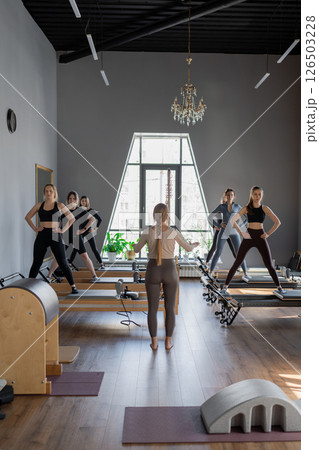 Young caucasian women exercising on pilates reformers in a bright studio. Their workout focuses on core strength and flexibility in a modern fitness environment. 126503228