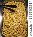 Golden french fries filling metal serving tray, crispy surface gleaming, black tongs resting alongside golden potatoes 126503314