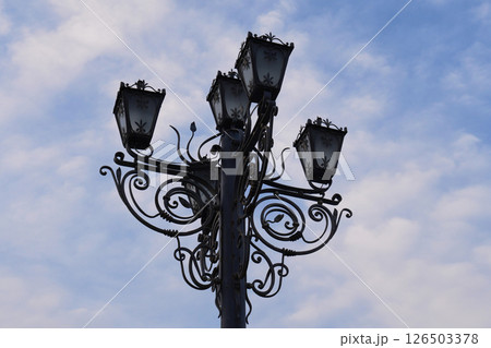 An intricate street lamp stands against a backdrop of clouds An intricate street lamp stands against a backdrop of clouds 126503378