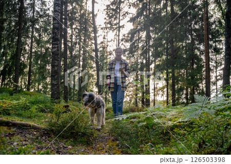 Woman walking dog in forest and using smartphone in sunlight forest Woman walking dog in forest and using smartphone in sunlight forest 126503398