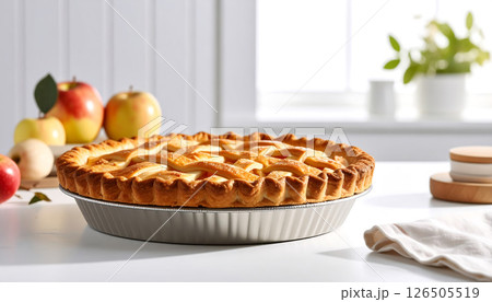 A homemade apple pie in a foil pan, with apples and baking ingredients on a white table. A homemade apple pie in a foil pan, with apples and baking ingredients on a white table. 126505519