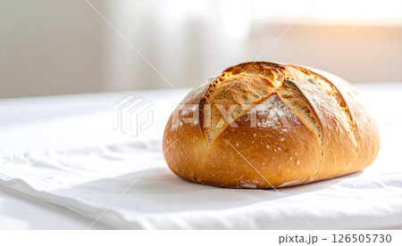 A rustic loaf of bread on a white cloth, with a bright background. 126505730