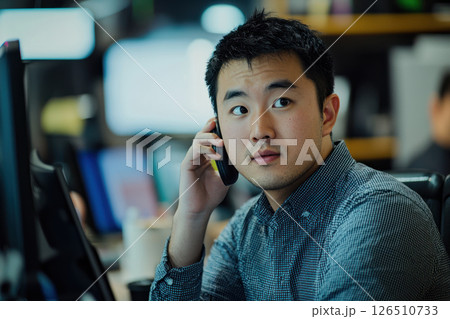 Young Asian professional on phone call in busy office environment, focused and engaged 126510733