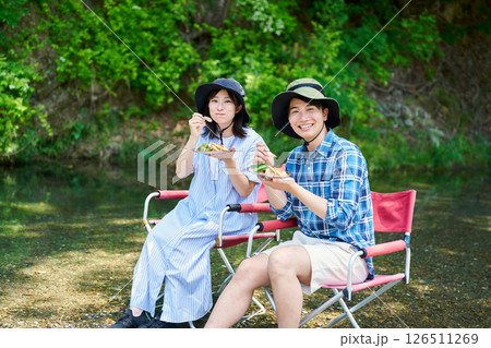 川辺でカレーを食べる男女 126511269