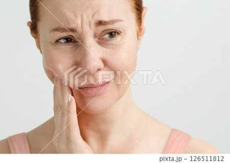 A woman suffers from severe toothache, she holds her hand to a sore tooth, her face is distorted. 126511812