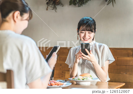 カフェでスマホを見ながら話す・おしゃべりする笑顔の若いアジア人女性たち 126512007