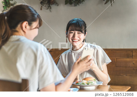 カフェでスマホを見ながら話す・おしゃべりする笑顔の若いアジア人女性たち カフェでスマホを見ながら話す・おしゃべりする笑顔の若いアジア人女性たち 126512008