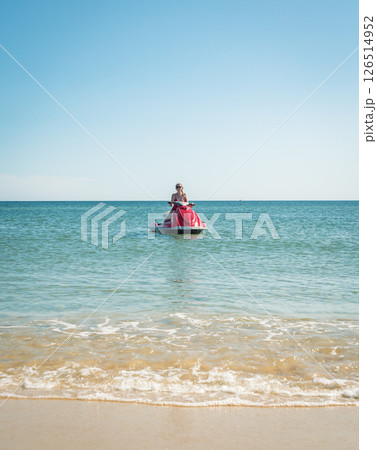 Woman enjoying a sunny day on a jet ski in clear blue ocean waters near a tropical beach 126514952