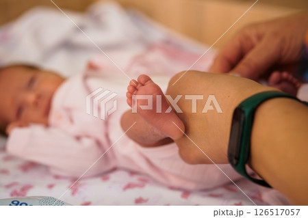 A tender moment featuring a newborn baby's tiny foot held by a caring hand, resting on a soft pink blanket, symbolizing new life and parental connection 126517057