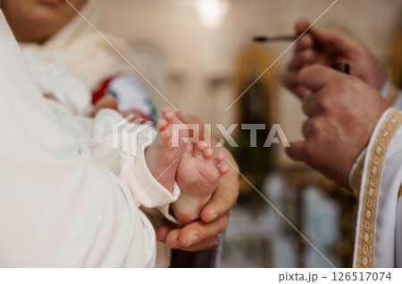 A tender moment during a baby's christening ceremony, where a priest anoints the infant's tiny foot with holy oil, symbolizing purification and acceptance into the faith A tender moment during a baby's christening ceremony, where a priest anoints the infant's tiny foot with holy oil, symbolizing purification and acceptance into the faith 126517074