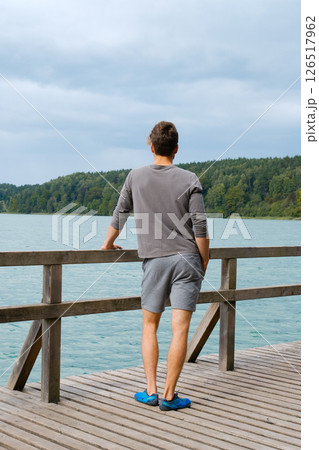 Young man standing near lake, view from back. Recreation in nature concept Young man standing near lake, view from back. Recreation in nature concept 126517962