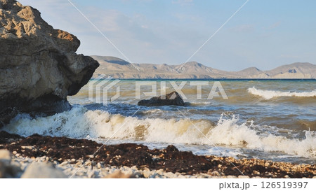 Waves crashing on Crimean rocky beach with mountains in background 126519397