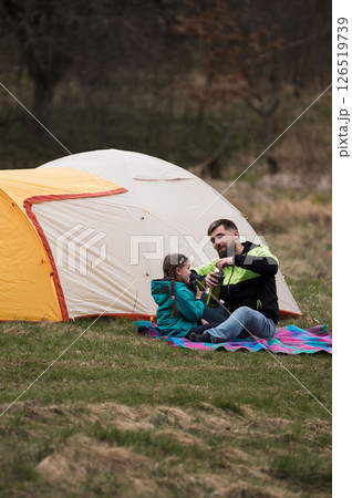 Father and daughter enjoying a cozy camping experience in nature during a serene afternoon at a picturesque campsite Father and daughter enjoying a cozy camping experience in nature during a serene afternoon at a picturesque campsite 126519739