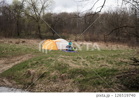 Enjoying a peaceful camping experience by the riverside with friends in a lush green setting during an overcast afternoon Enjoying a peaceful camping experience by the riverside with friends in a lush green setting during an overcast afternoon 126519740