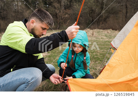 Setting up a tent with a young girl in a lush green field during a sunny day, creating cherished memories in nature while enjoying quality time together 126519845