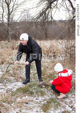 Two individuals engage in nature exploration during a chilly winter day in a serene, snowy landscape with bare trees and gentle earth tones 126520034