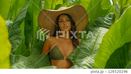 A woman in a large hat surrounded by vibrant green leaves, highlighting beauty and nature 126520296