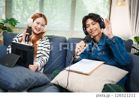 Friendly podcast hosts waving at camera with microphones and headphones 126521211