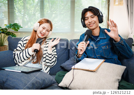Friendly podcast hosts waving at camera with microphones and headphones Friendly podcast hosts waving at camera with microphones and headphones 126521212