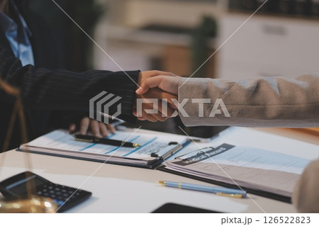 Lawyer shaking hands with a client making about documents, contracts, agreements, cooperation agreements with a female client at the lawyer's desk and a hammer at the table. Lawyer shaking hands with a client making about documents, contracts, agreements, cooperation agreements with a female client at the lawyer's desk and a hammer at the table. 126522823