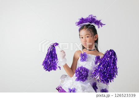 Smiling cheerleader girl wearing purple and white outfit with pom-poms. Studio portrait exuding energy and joy against a white background. cheerleader kid 126523339