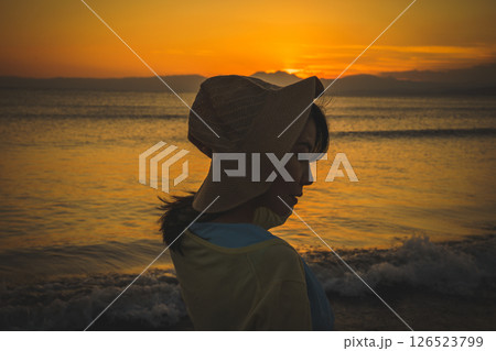 夕焼けの海を眺める麦わら帽子の女性 126523799