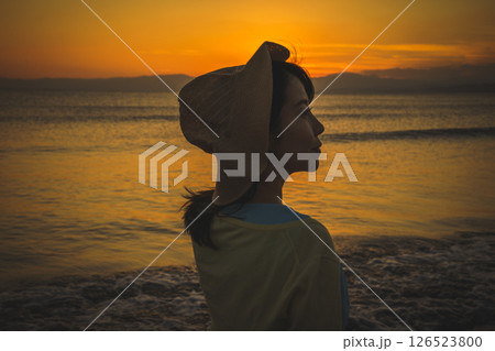 夕焼けの海を眺める麦わら帽子の女性 126523800