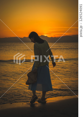 夕焼けの海辺を散策する女性 126524091