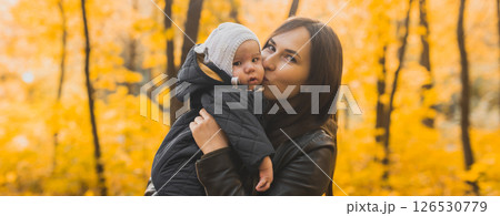 Banner Autumn scene of mother kissing young baby girl outdoors with colorful trees in park. Copy space Banner Autumn scene of mother kissing young baby girl outdoors with colorful trees in park. Copy space 126530779