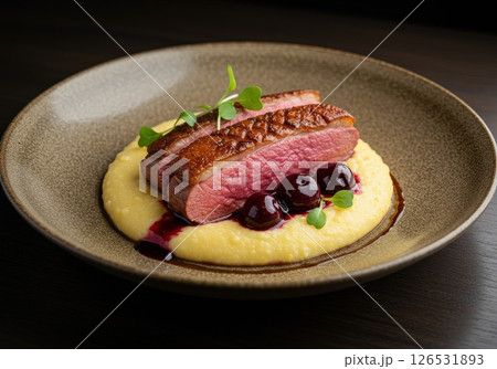 Pan seared duck breast slices with crispy skin served on creamy polenta with cherry sauce 126531893