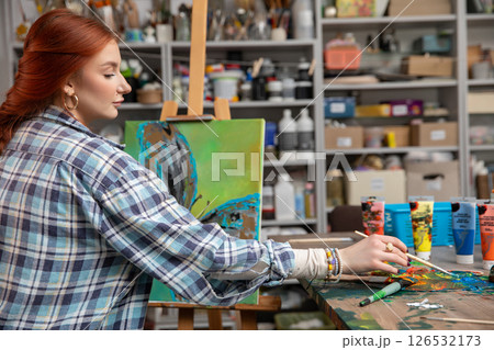 A Creative and Young Artist in a Colorful, Vibrant Studio Engaged in Painting Artworks 126532173