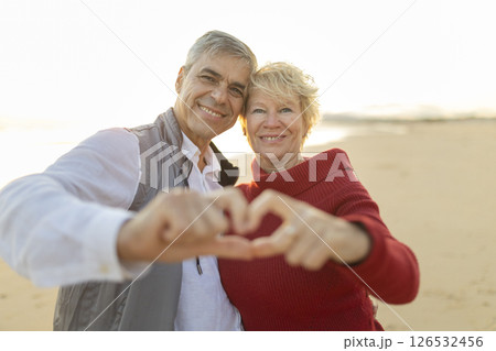 Happy senior couple making heart shape with hands on beach at sunset 126532456