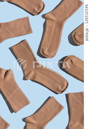 Arrangement of beige socks on light blue surface, highlighting different textures and styles, perfect for fashion, textile design, and creative projects. Vertical 126532548