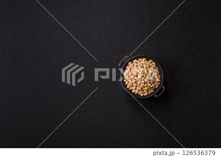 Peeled pine nuts in a bowl on a dark concrete background Peeled pine nuts in a bowl on a dark concrete background 126536379