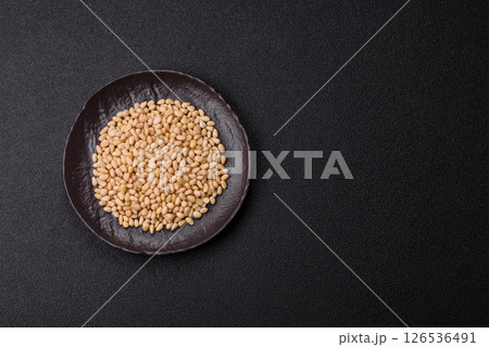 Peeled pine nuts in a bowl on a dark concrete background 126536491