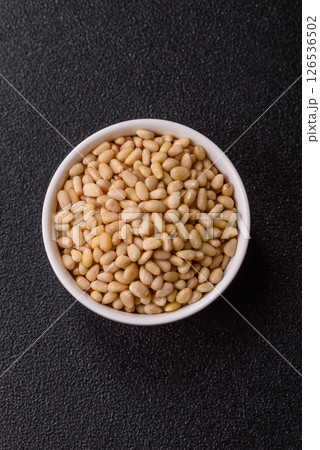 Peeled pine nuts in a bowl on a dark concrete background 126536502