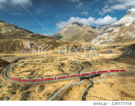 Aerial view of modern red train, alpine mountains, orange meadows Aerial view of modern red train, alpine mountains, orange meadows 126537359