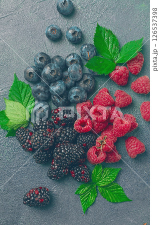 a mix of ripe berries, with leaves scattered on the table, raspberries, blackberries, blueberries, food background, 126537398