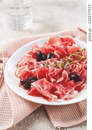 Freshly cut dried meat, served with olives and herbs, on a white plate, light background, no people, 126537423