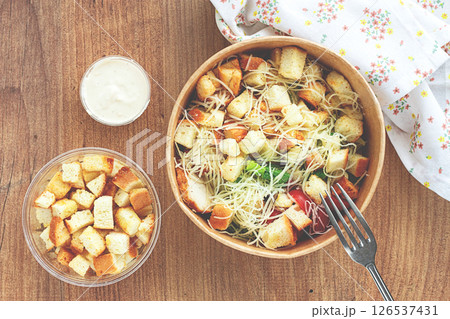 Caesar salad in a paper container, take it on the way, with sauce and croutons, on the table, snack, no people, 126537431