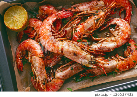 Juicy grilled shrimp, placed on a baking sheet lined with parchment paper, garnished with herbs and lemon. 126537432