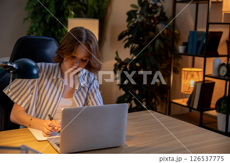 A Focused Young Woman Engaged in Working on Her Laptop in a Modern Home Office Environment A Focused Young Woman Engaged in Working on Her Laptop in a Modern Home Office Environment 126537775