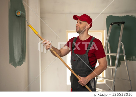 Painter using roller applying green paint on wall in house renovation 126538016