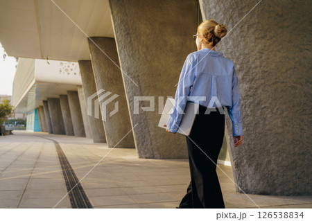 A businesswoman walks confidently in a modern city, showcasing her professional style 126538834
