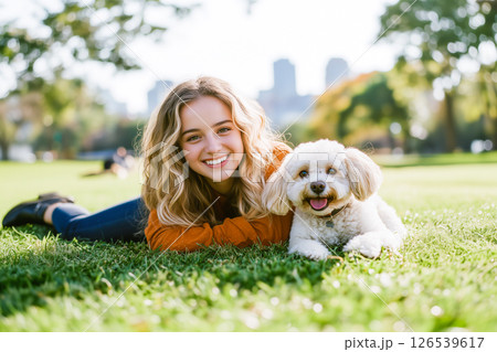 A woman and her dog are laying on the grass in a park 126539617