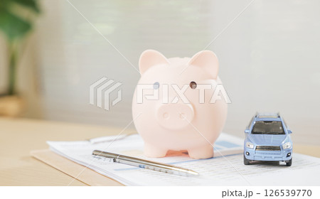 A car piggy bank with a pen and banking book symbolizes saving money, finance planning, and business growth. Highlights success, retirement savings, and insurance strategies for financial stability. 126539770