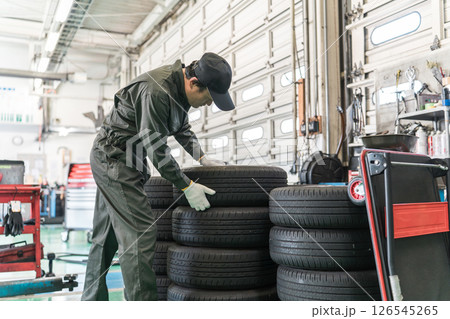 整備工場でタイヤを移動する自動車整備士・メカニックの中年アジア人男性 整備工場でタイヤを移動する自動車整備士・メカニックの中年アジア人男性 126545265