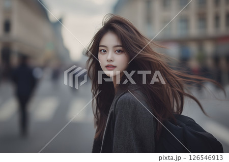 Woman with long brown hair is standing on a street 126546913